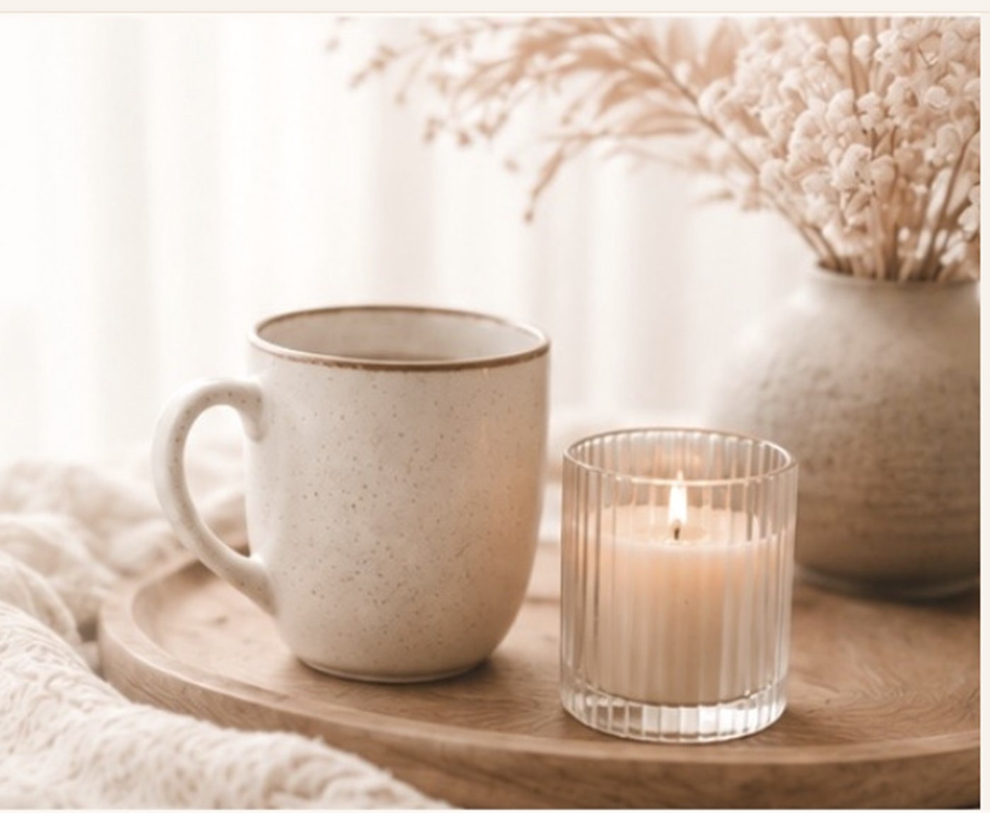 Tasse, Kerze und eine Vase mit Trockengräsern auf einem Holztablett.