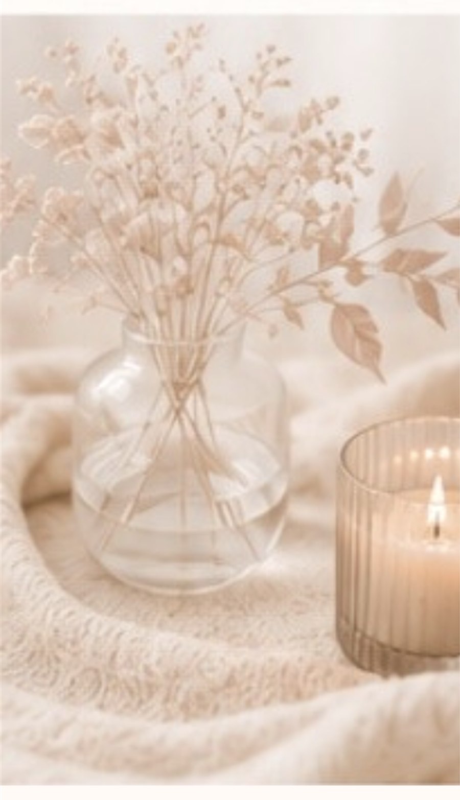 Glasvase mit hellen Trockenblumen und Blättern in warmem, weichem Licht.